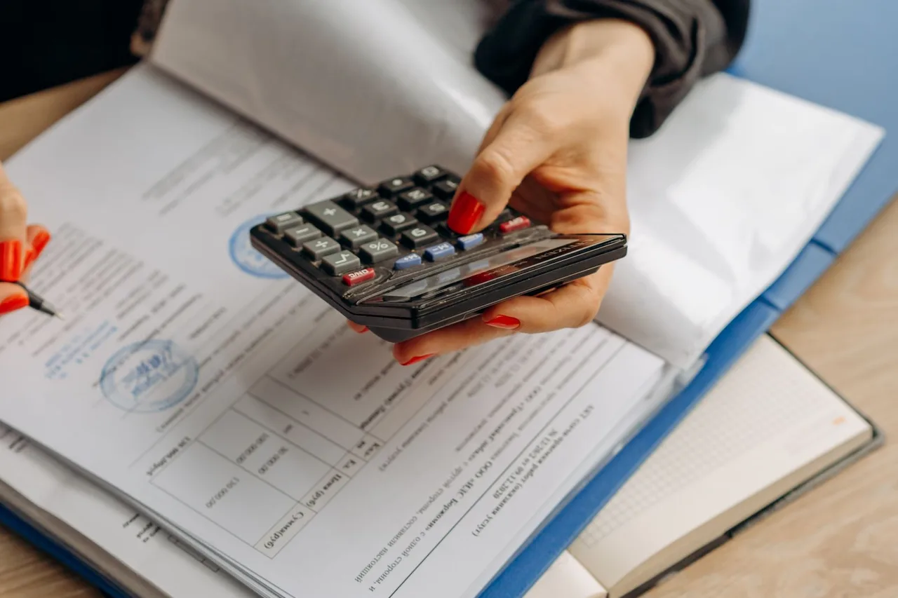 A person checking financial paperwork with a calculator