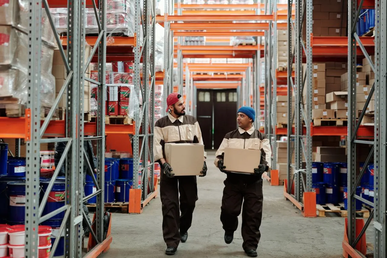 Two warehouse workers carrying boxes along storage shelves